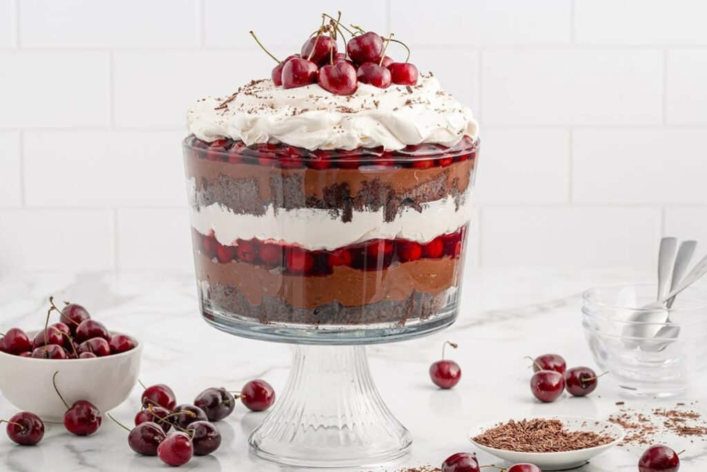 Black Forest trifle layered with chocolate cake, whipped cream, and cherries in a glass dish.