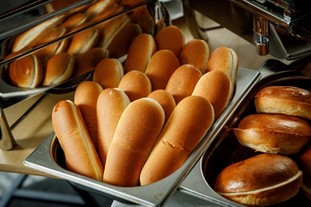 Burger buns and hotdog buns displayed in a stainless-steel tray.