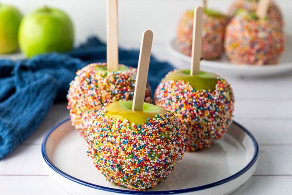 Caramel apples on sticks arranged on a plate.