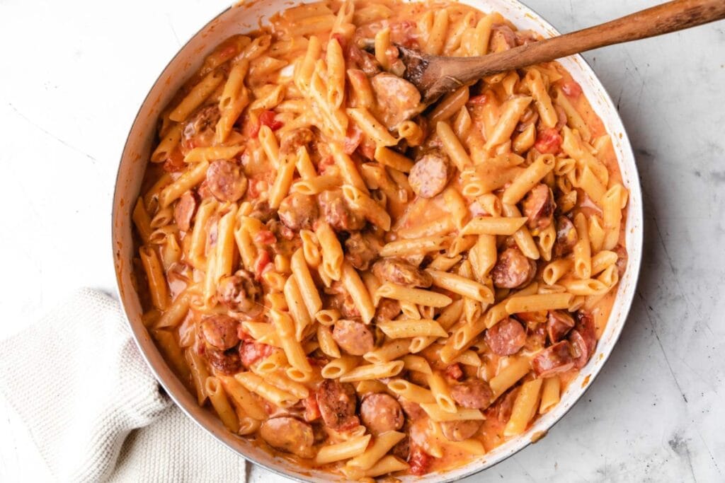 Cheesy kielbasa pasta with sausage slices in a skillet.