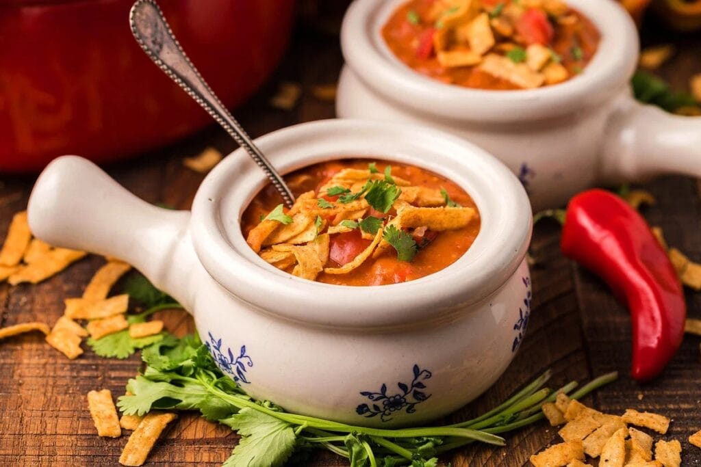 Chicken enchilada soup in a handled bowl topped with tortilla strips and cilantro.