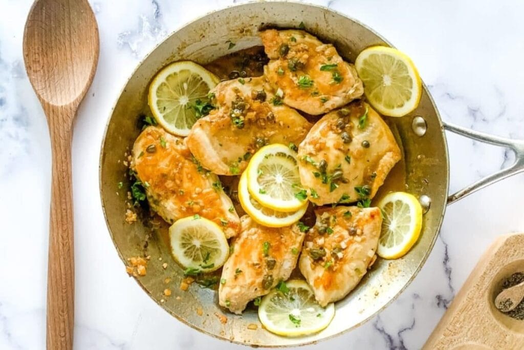 Chicken piccata with lemon slices and capers in a skillet.