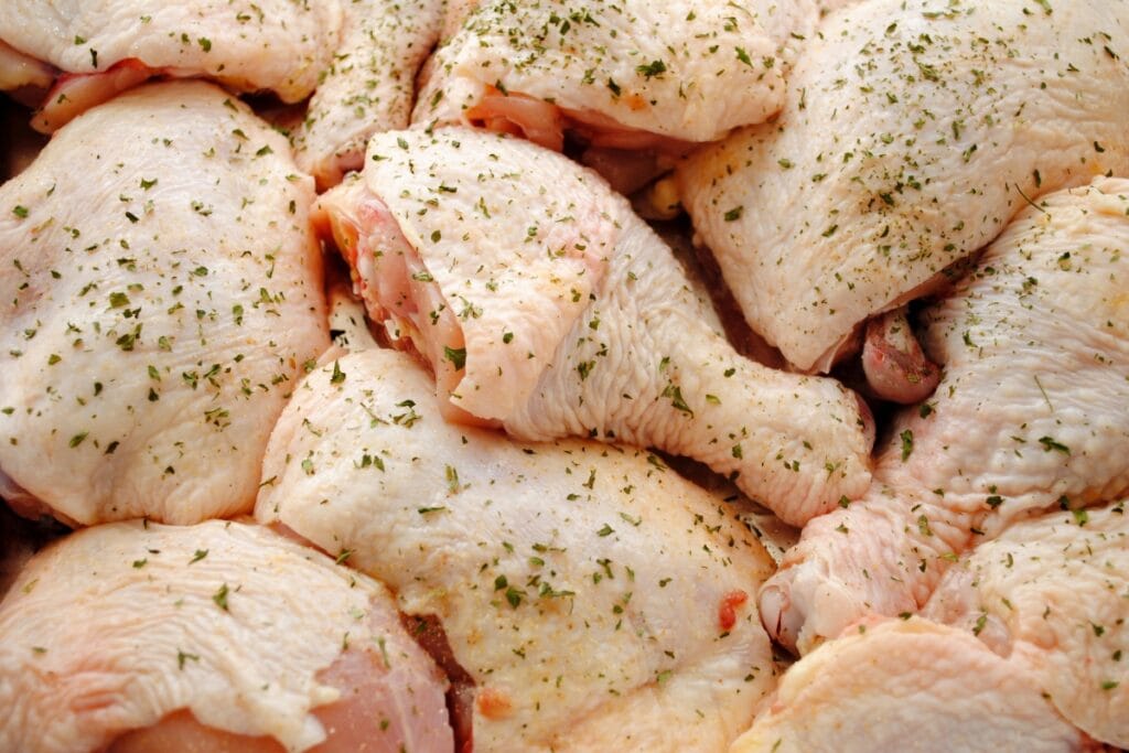 Uncooked chicken legs and thighs with skin, sprinkled with herbs and spices.