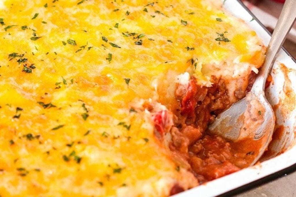 Chili mashed potato casserole with melted cheese in a baking dish with a spoon.