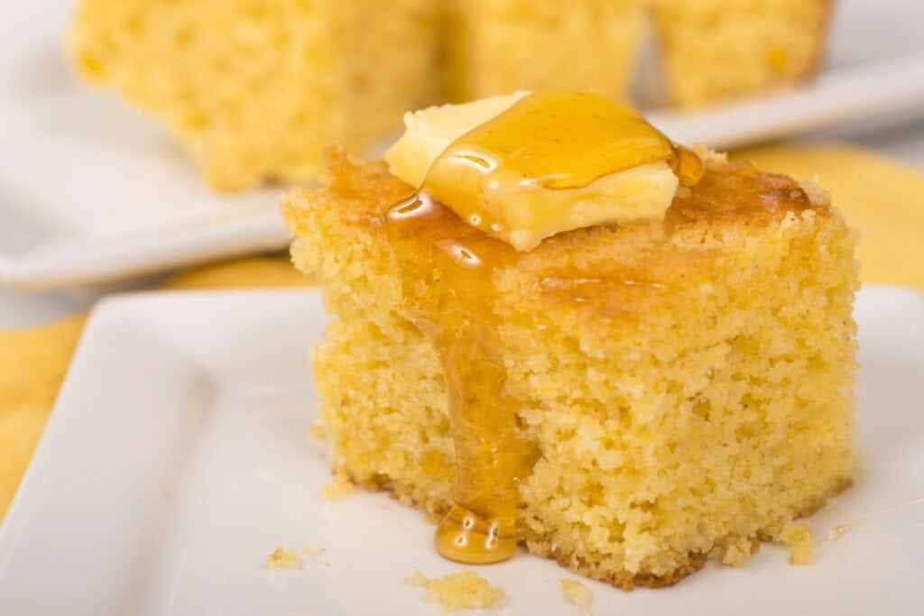 Slice of cornbread on a plate topped with butter and drizzled with honey.