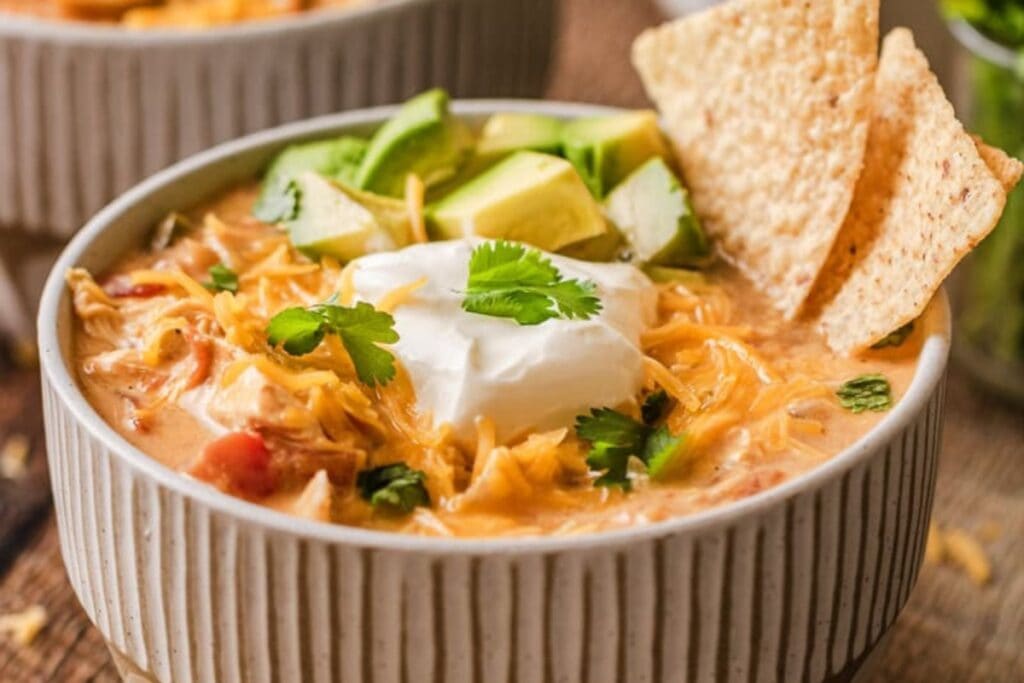 Creamy chicken fajita soup in a bowl topped with avocado and tortilla chips.