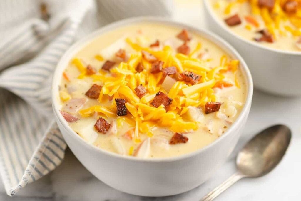 Creamy ham and potato soup in a bowl topped with crispy ham and cheese.