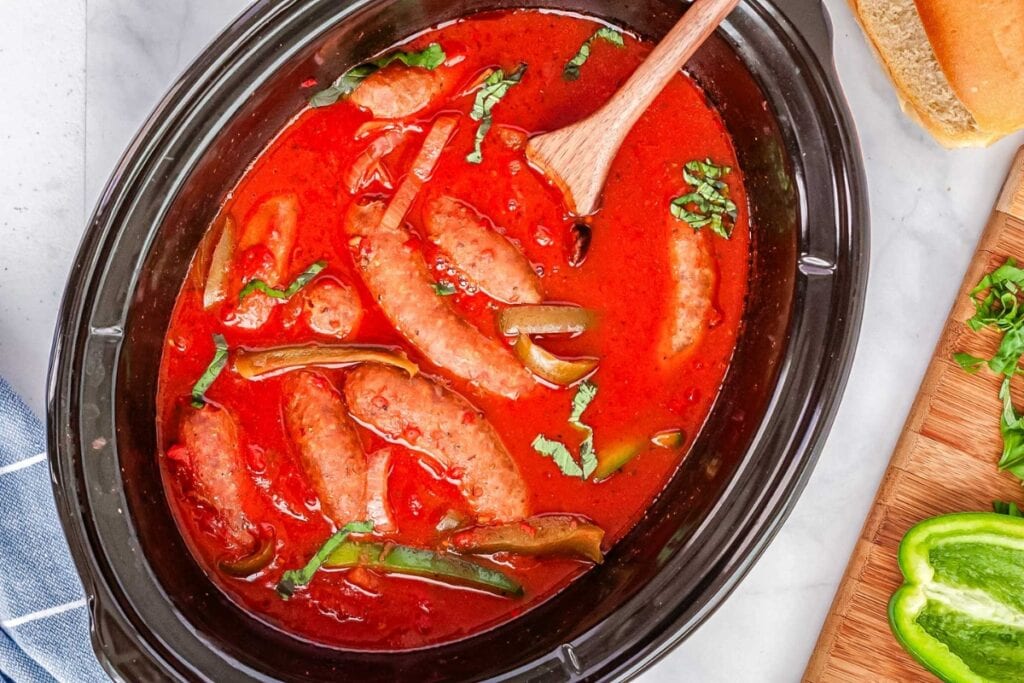 Crock Pot sausage and peppers in tomato sauce with a wooden spoon.