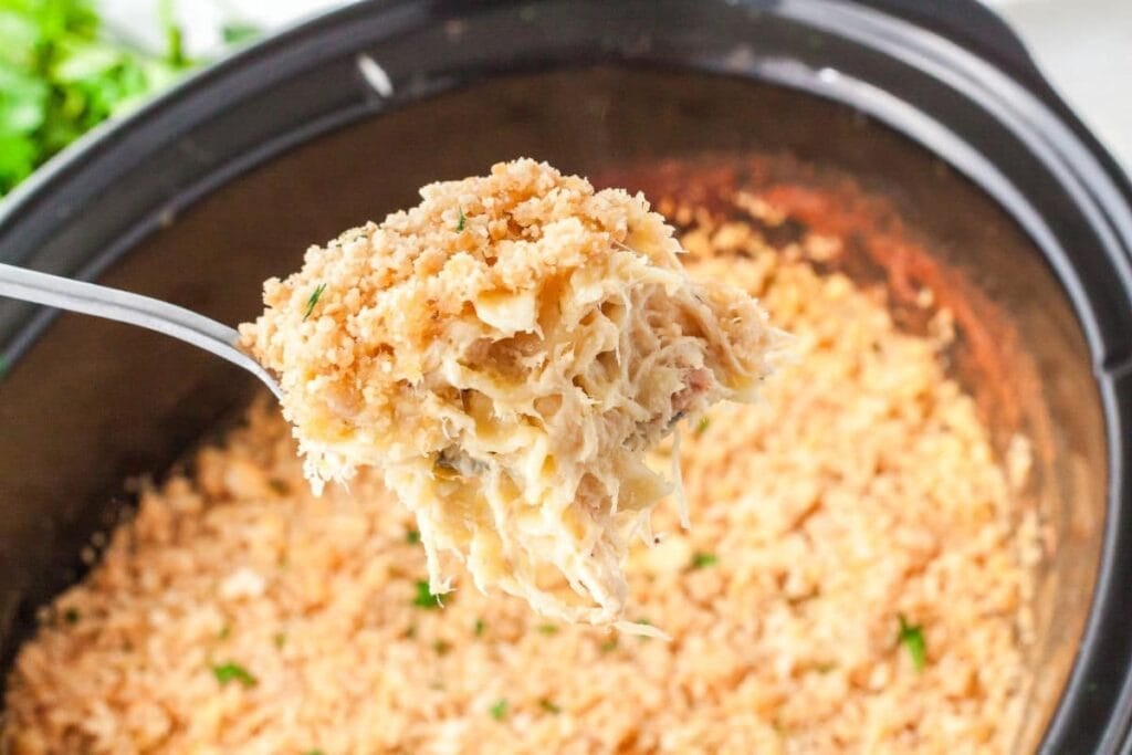 Crockpot chicken noodle casserole with breadcrumbs on a spoon over a slow cooker.