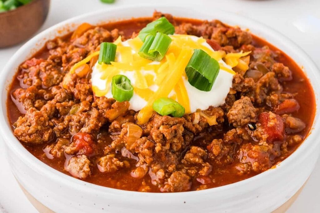 Close-up of Crockpot Chili Without Beans topped with cheese, sour cream, and green onions in a bowl.