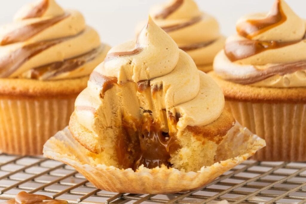Dulce de leche cupcakes with creamy caramel filling and swirled frosting on a cooling rack.
