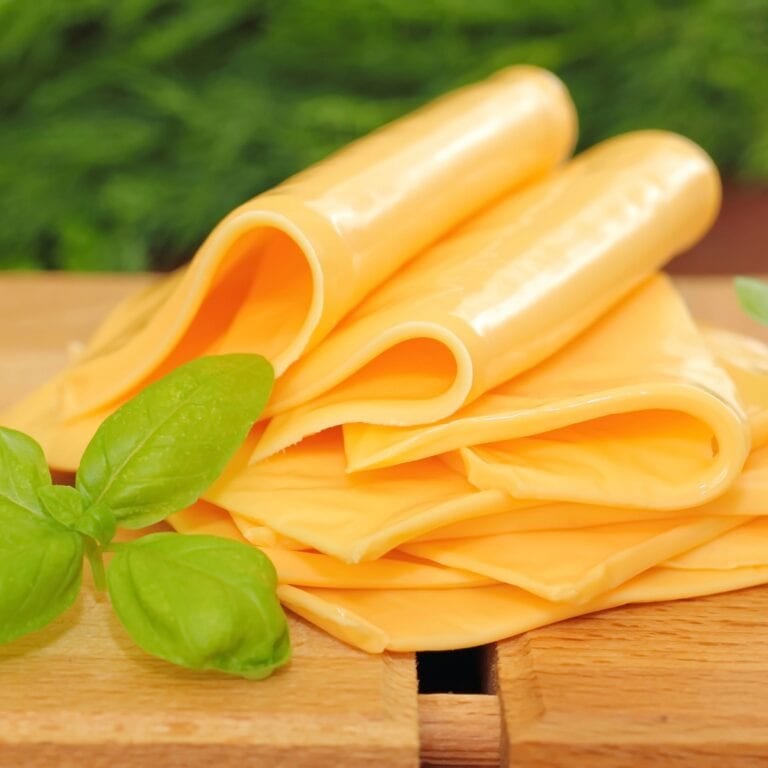 Sliced processed cheese on a wooden cutting board.