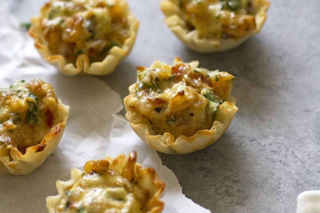 French onion tartlets with flaky crusts on parchment paper.