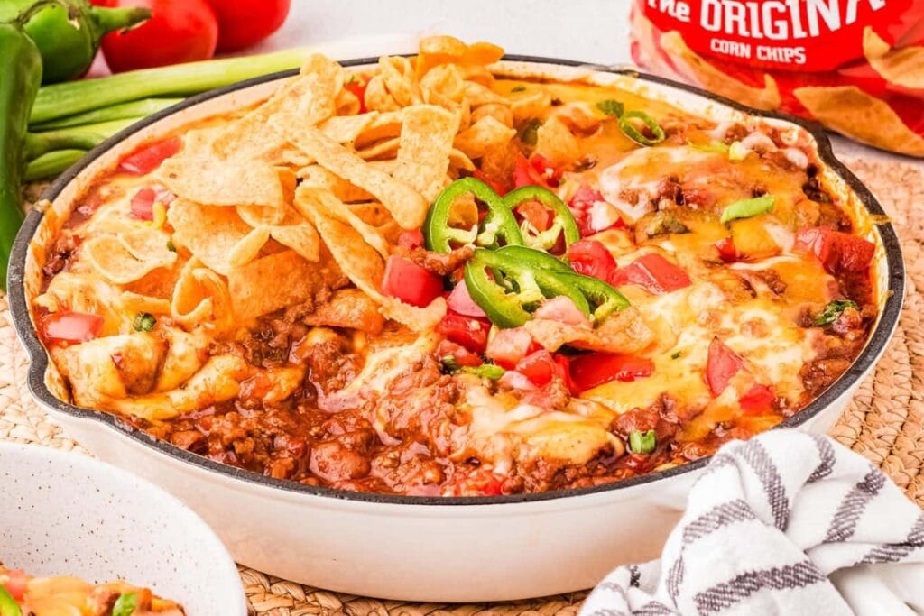 “Frito pie topped with melted cheese, chili, and corn chips in a bowl.