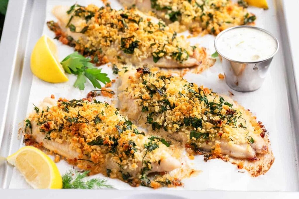 Lemon baked fish with herbs and lemon slices on a sheet pan.