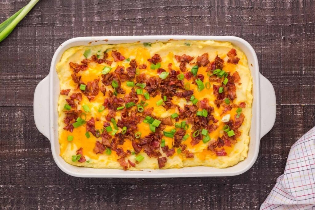 Mashed potatoes in a baking dish topped with cheese, bacon, and green onions.