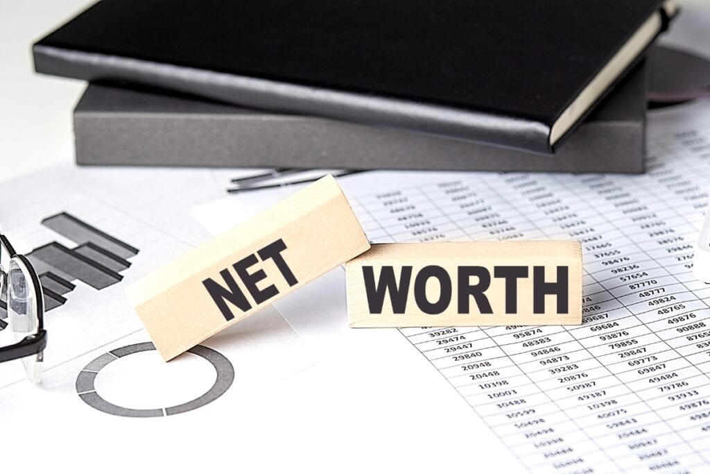 Wooden blocks with the words net worth on financial documents.