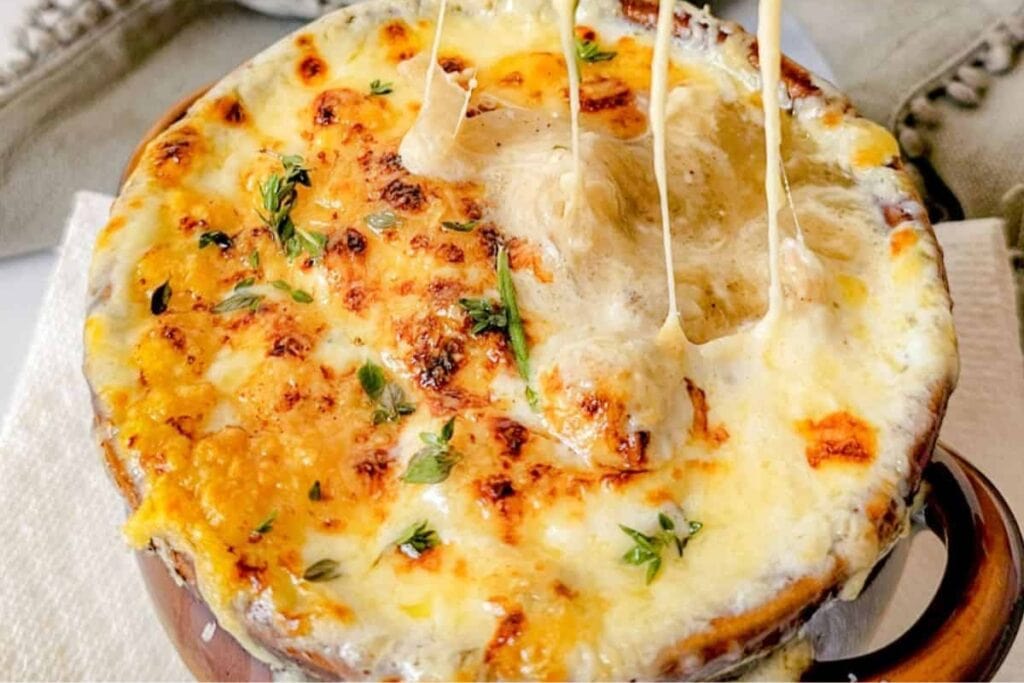 Close-up of Normandy French onion soup in a handled bowl.