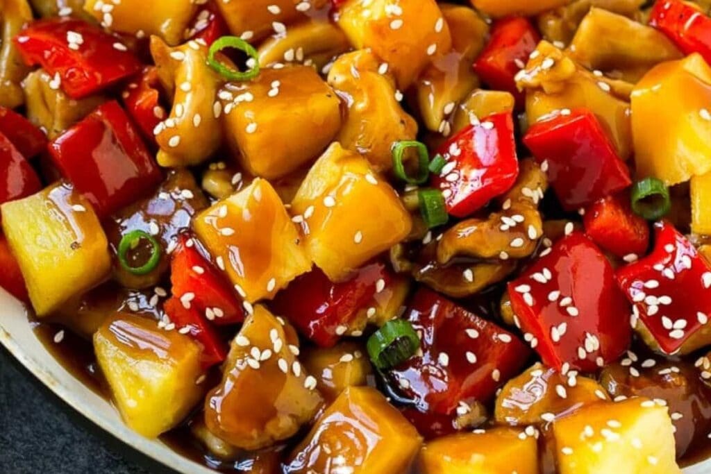 Pineapple chicken with bell peppers and pineapple chunks in a skillet.