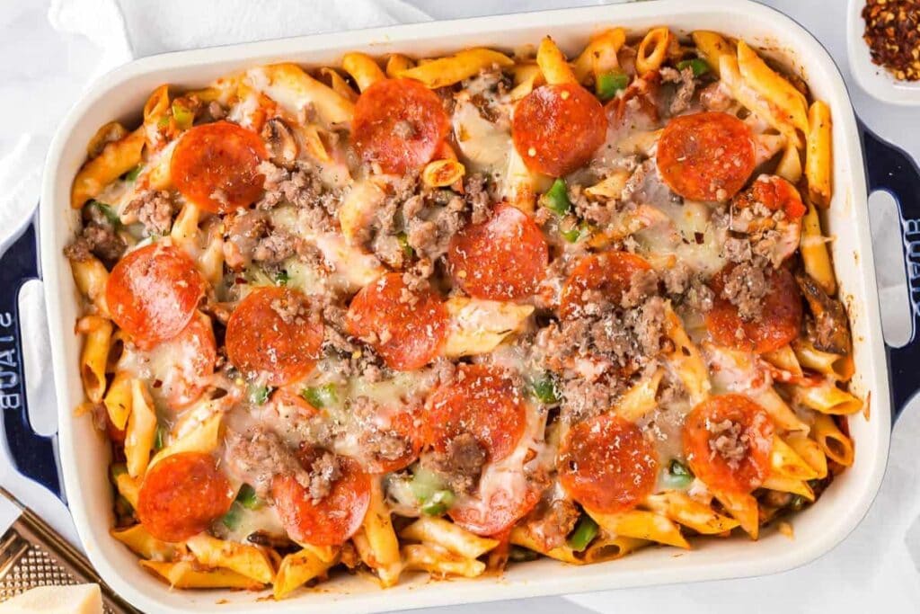 Pizza pasta casserole topped with melted cheese and pepperoni in a baking dish.