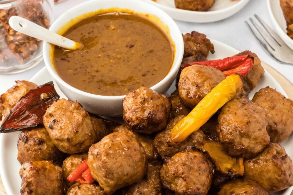 Sausage and peppers on a plate with dipping sauce.