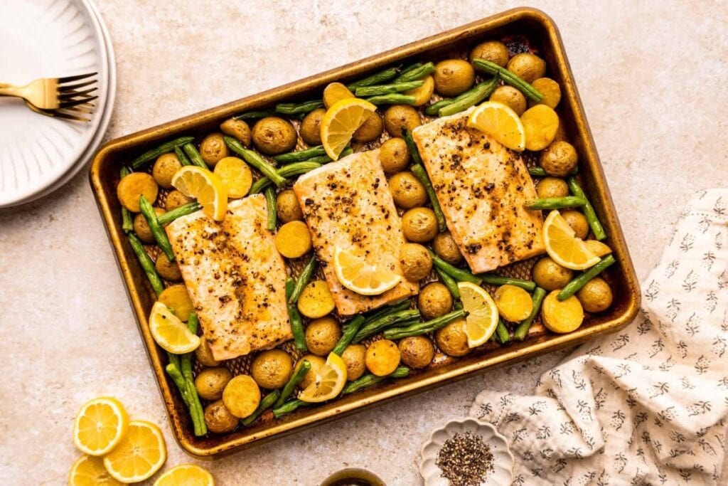 Sheet pan lemon pepper salmon with roasted vegetables and lemon slices.