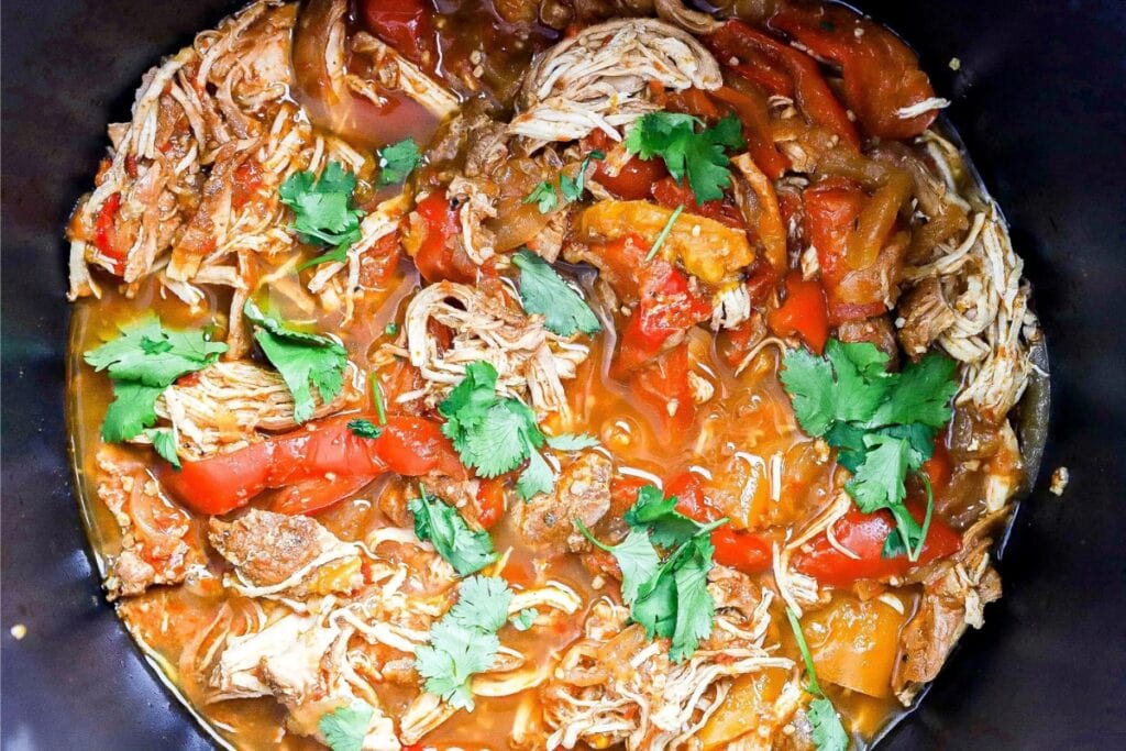 Chicken fajitas with bell peppers and onions cooking in a slow cooker.