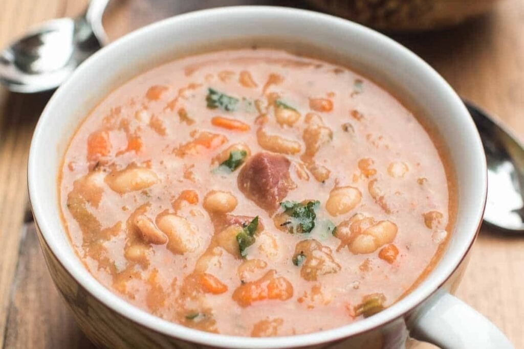 Close-up of ham and bean soup served in a cup with a handle.