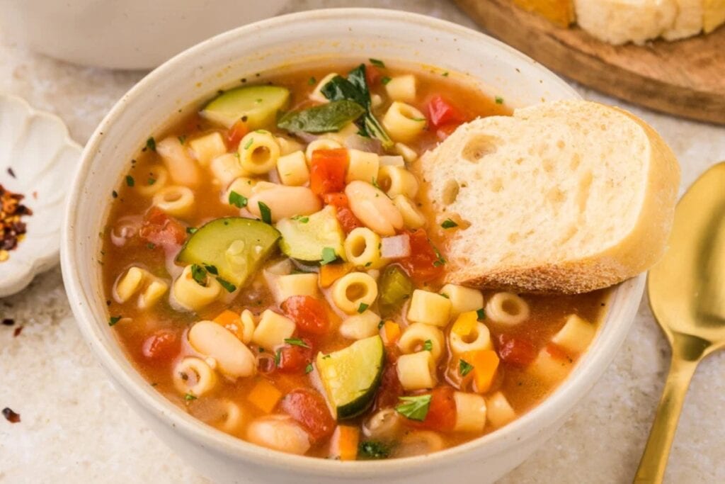 Stovetop minestrone soup in a bowl with a slice of bread.