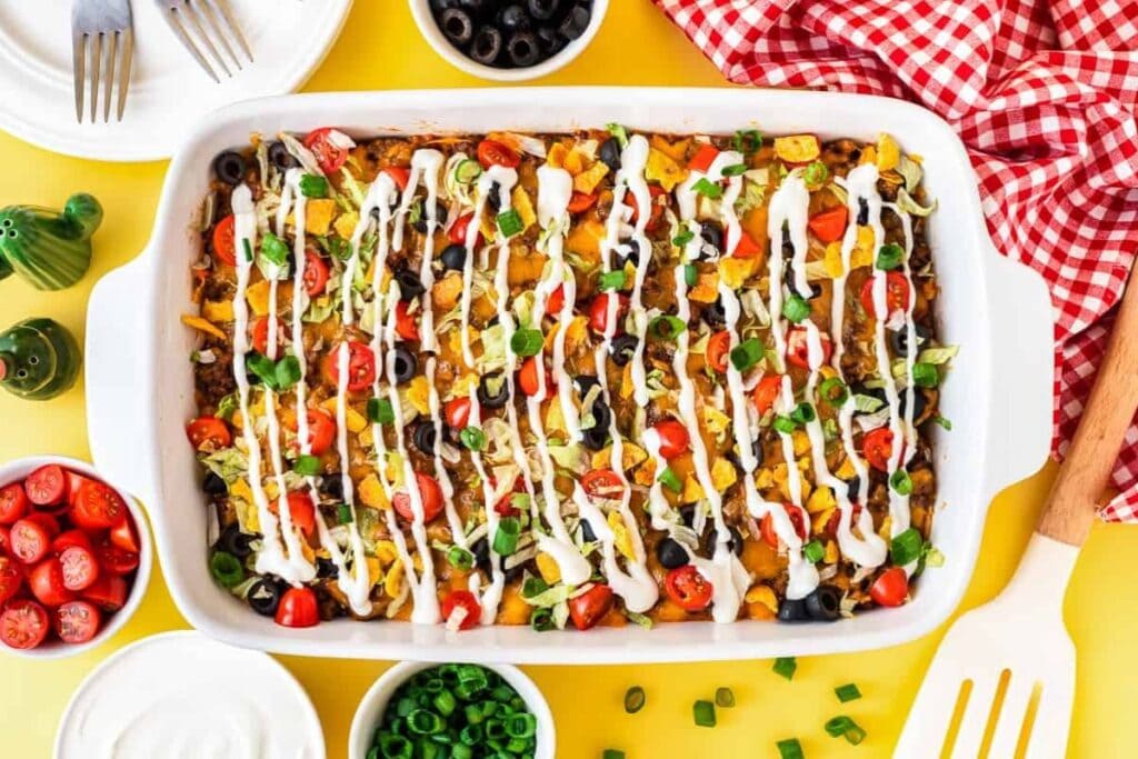 Taco casserole topped with melted cheese, lettuce, and tomatoes in a baking dish.