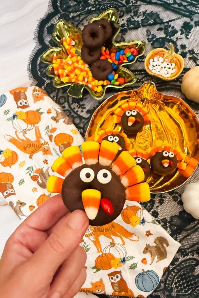 Hand holding a finished turkey-shaped donut with candy corn feathers.