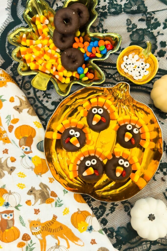 Five decorated turkey donuts with candy corn feathers arranged on a pumpkin-shaped plate.