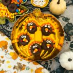Five decorated turkey donuts with candy corn feathers arranged on a pumpkin-shaped plate.