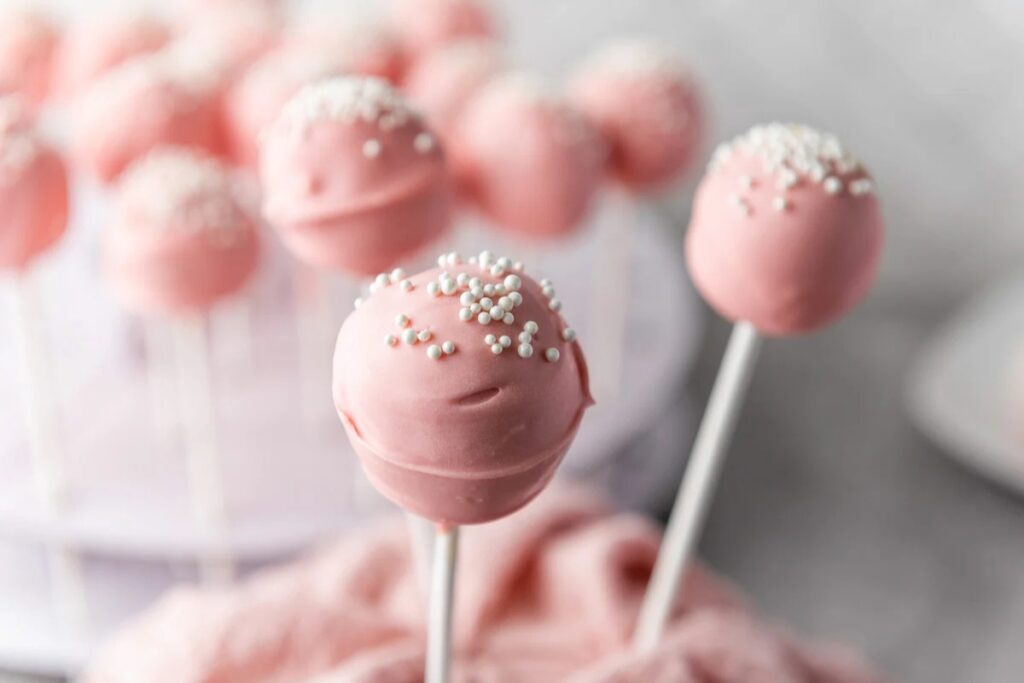 Vanilla cake pops on sticks topped with white sprinkles.