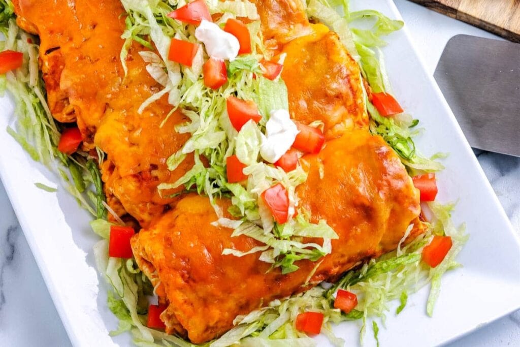 Wet burritos topped with red sauce and melted cheese on a plate.