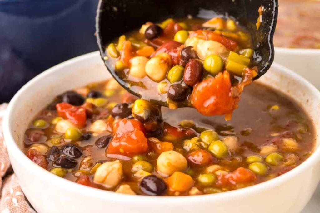 7 Can Soup in a bowl with a ladle lifting mixed beans and vegetables.