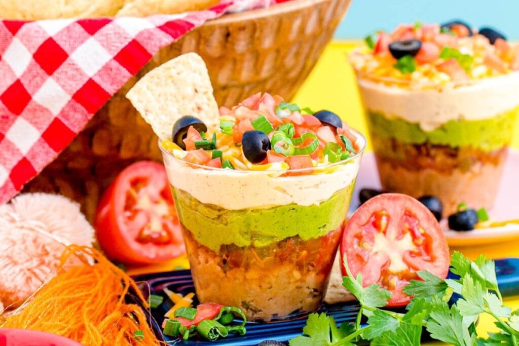 Individual 7-layer dip cups with beans, guacamole, sour cream, cheese, salsa, and olives.