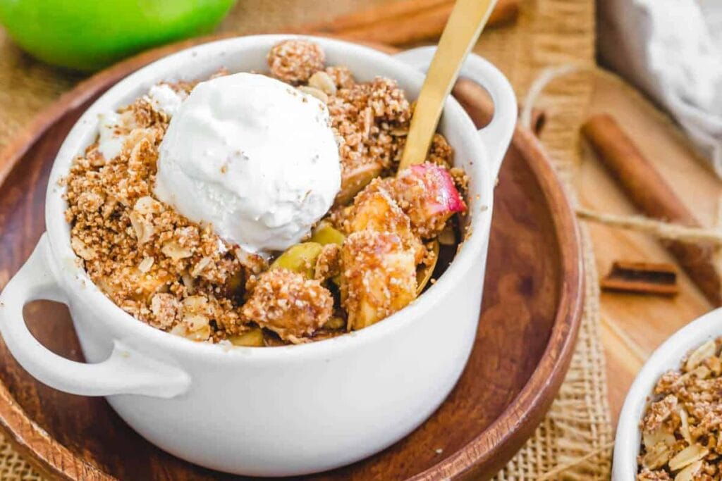 Apple crisp with a scoop of ice cream in a white bowl with a gold spoon.