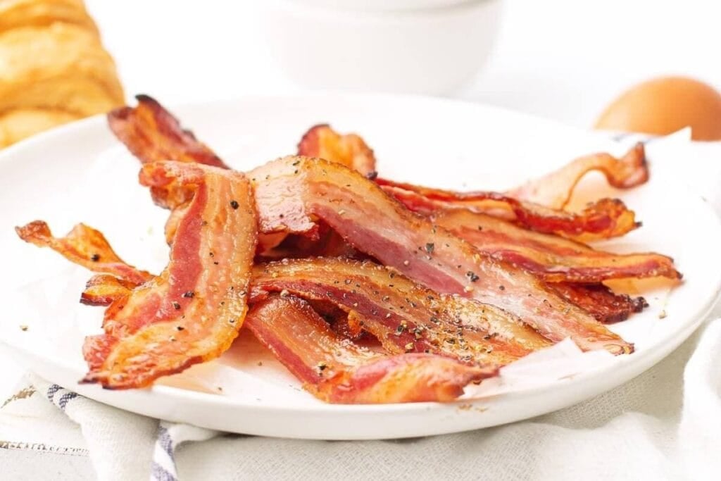 Cooked bacon strips on a white plate.