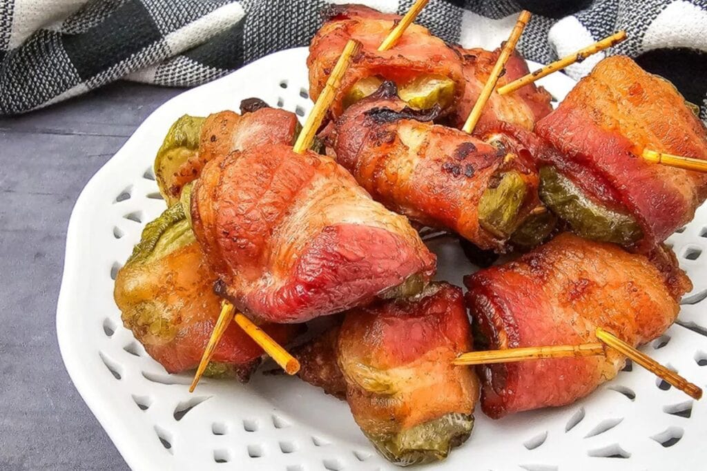 Bacon-wrapped pickle bites on a white plate with toothpicks.