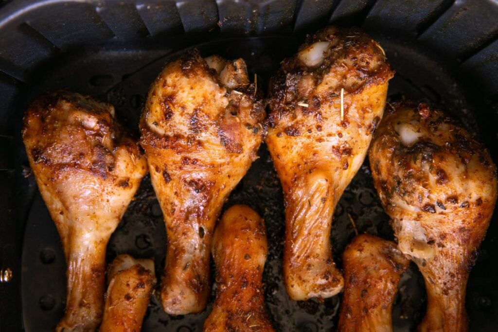 Four seasoned chicken drumsticks inside an air fryer basket.