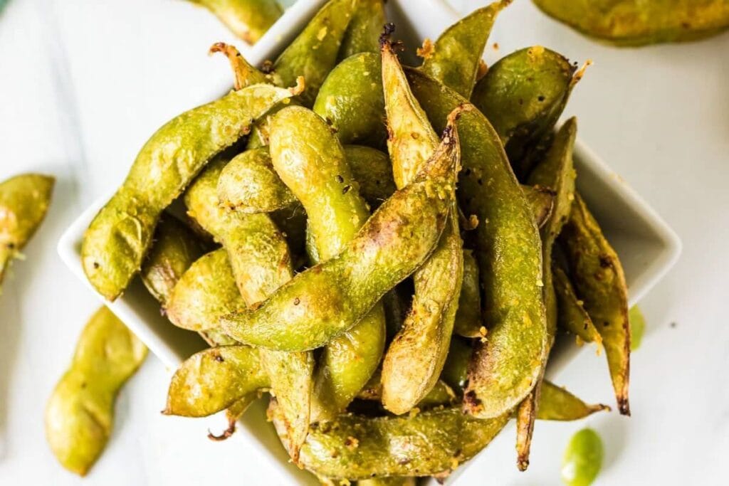 Close-up of air-fried edamame in a white bowl, seasoned with spices.