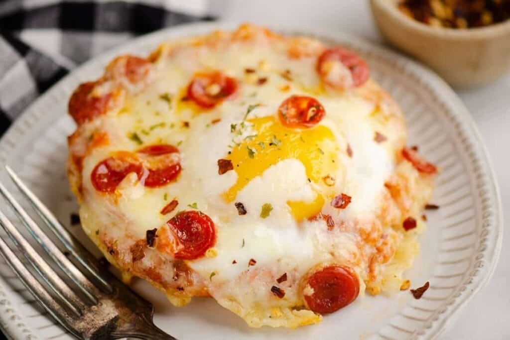 English muffin breakfast pizza with egg, cheese, and pepperoni on a plate.