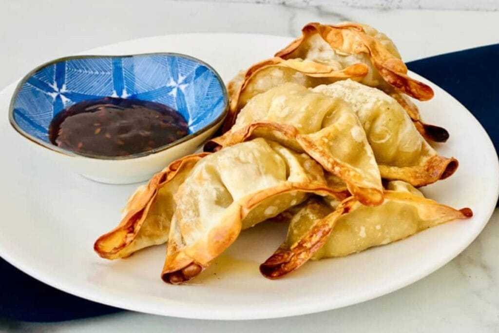 Air-fried potstickers with dipping sauce in a blue and white bowl on a plate.