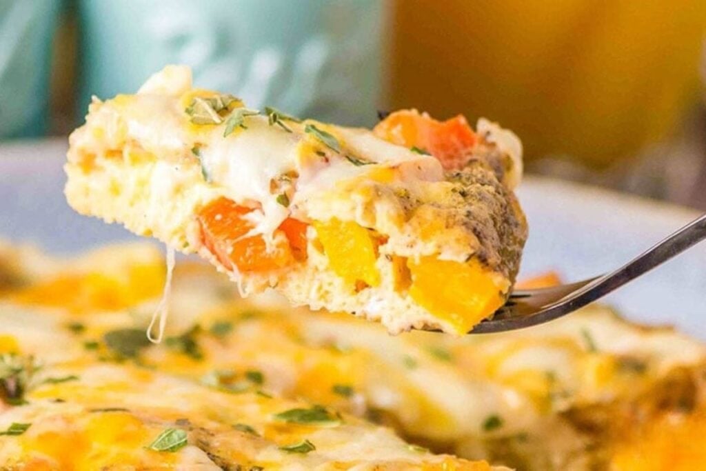A slice of omelette with cheese and diced vegetables on a fork.