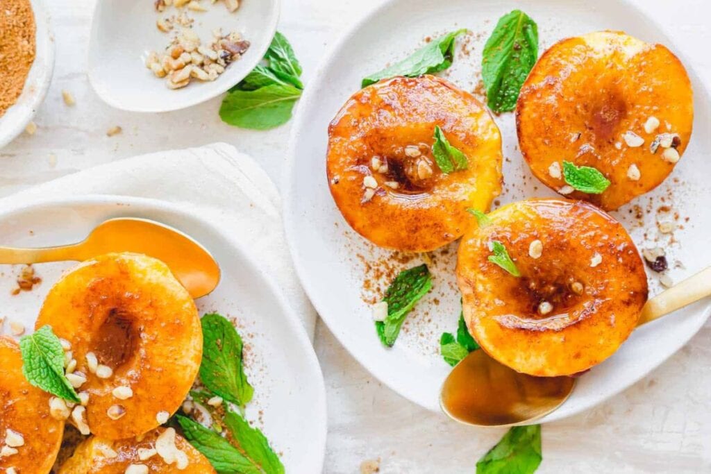 Air-fried peaches with nuts and mint on white plates, with golden spoons.