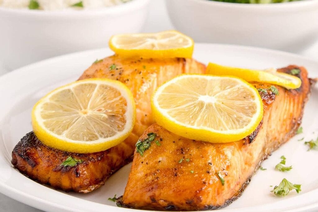 Two salmon fillets on a plate, garnished with lemon slices and parsley.