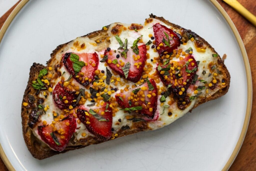 Toast topped with melted cheese, sliced strawberries, herbs, and seasonings.