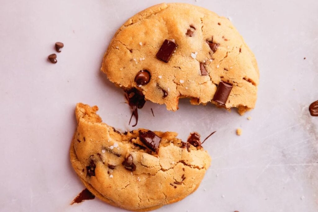 Broken chocolate chip cookie with melted chocolate on a light surface.