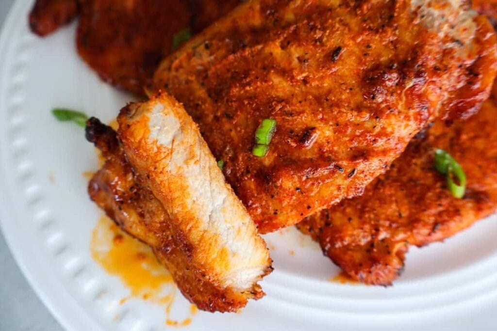 Air-fried pork chops with a reddish-brown seasoning on a white plate.